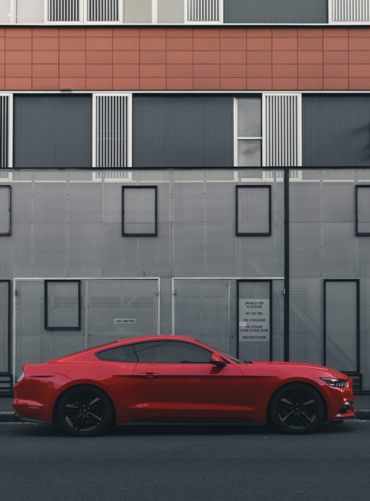 Sleek Red Car Side View Against Modern Geometric Building Wallpaper