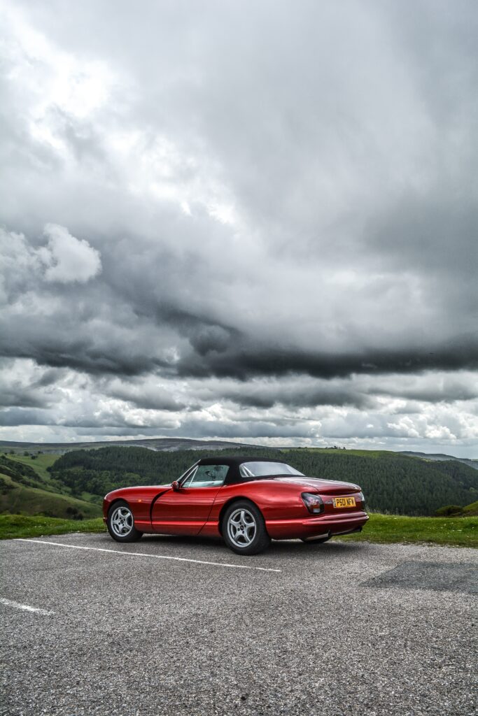 Sleek Red Convertible Amidst Lush Greenery: Dramatic Background Wallpaper