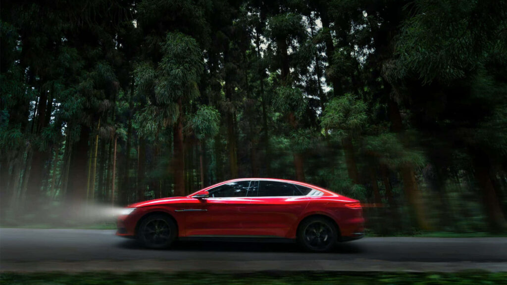 Red sedan speeding through dense forest with headlights cutting shadows wallpaper background
