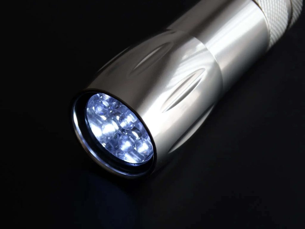 Sleek silver flashlight with bright LED light on black background minimalist wallpaper