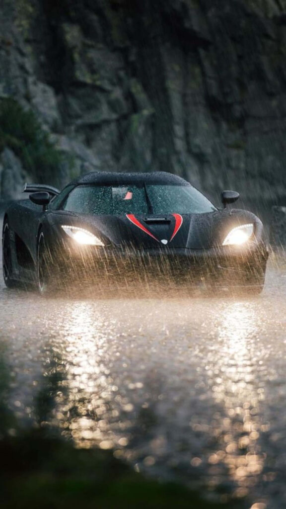 Sleek sports car speeding through rainy night wet road headlights reflecting rocky backdrop wallpaper