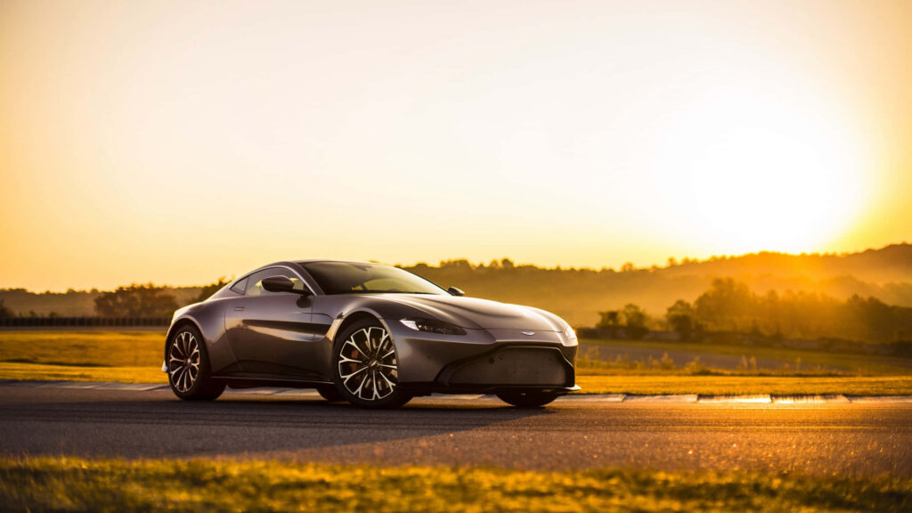 Sleek sports car glowing under golden sunset on open road with sharp design powerful presence Wallpaper