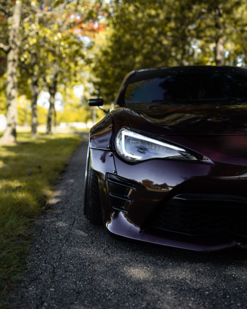 Sleek Sports Car Headlight on Scenic Leafy Road - Stunning Wallpaper