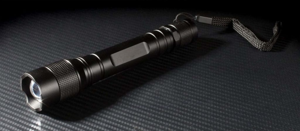 Sleek black LED tactical flashlight on dark carbon fiber surface macro tech wallpaper background