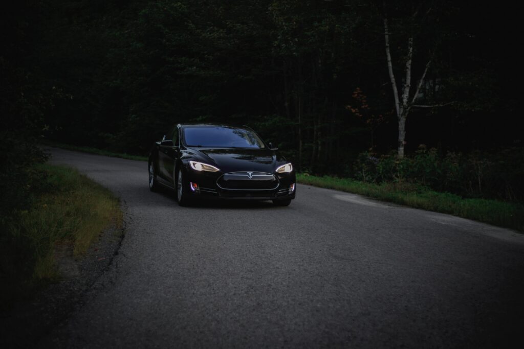 Sleek Tesla Car on Winding Road Through Shadowy Forest Wallpaper