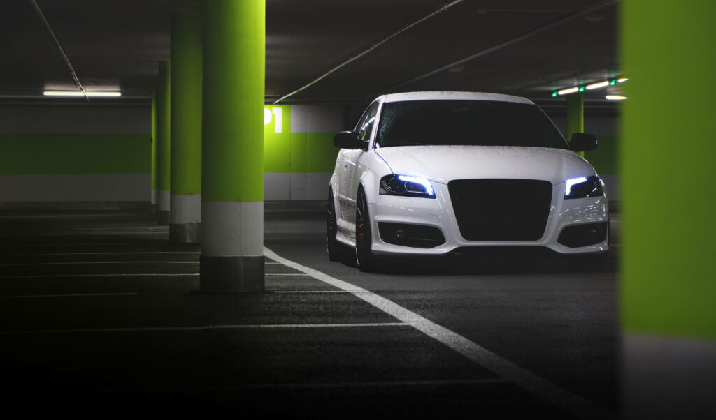 White Audi with sharp LED headlights illuminated in neon-lit modern parking lot at night Wallpaper