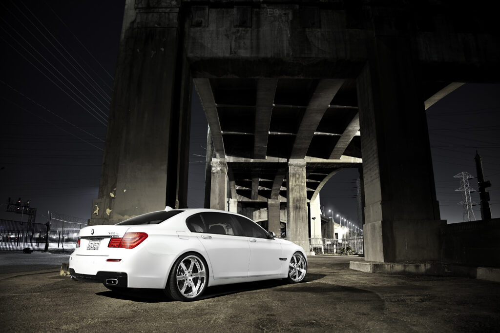 Sleek White BMW 750Li Rear View Under Industrial Structure - Urban Elegance Wallpaper