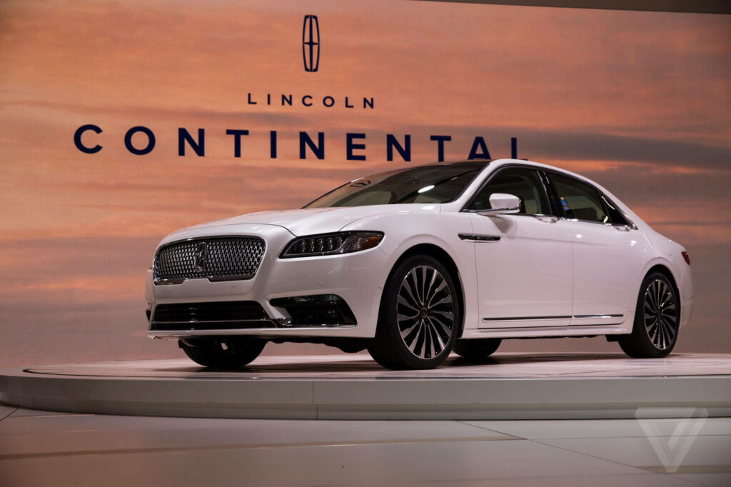 White Lincoln Continental on rotating platform at Detroit Auto Show with Lincoln logo backdrop Wallpaper