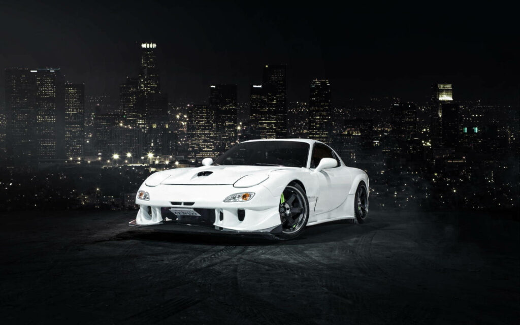 White Mazda RX7 parked at night with vibrant illuminated city skyline backdrop urban scene wallpaper