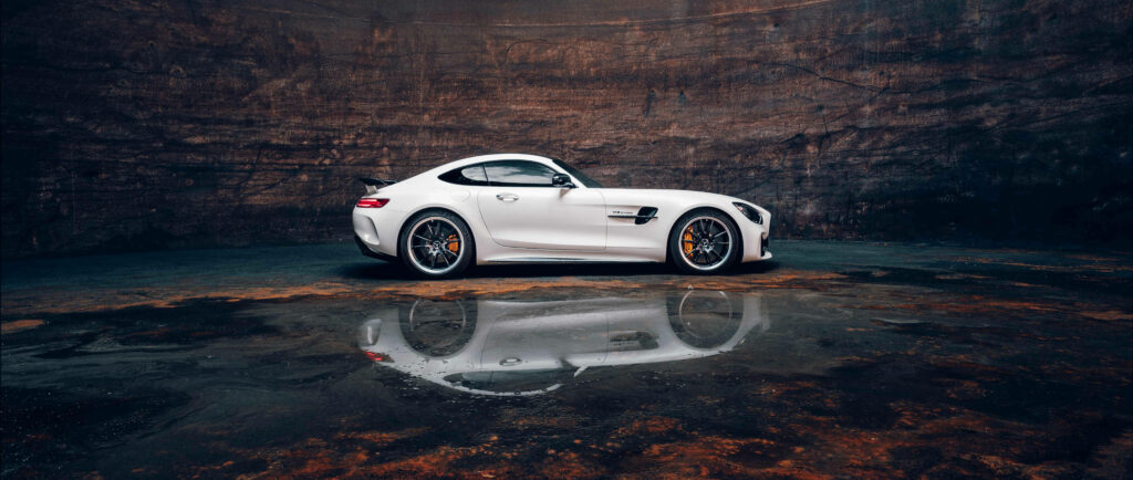 White Mercedes AMG parked inside rugged cave with glossy wet floor reflection 4K wallpaper