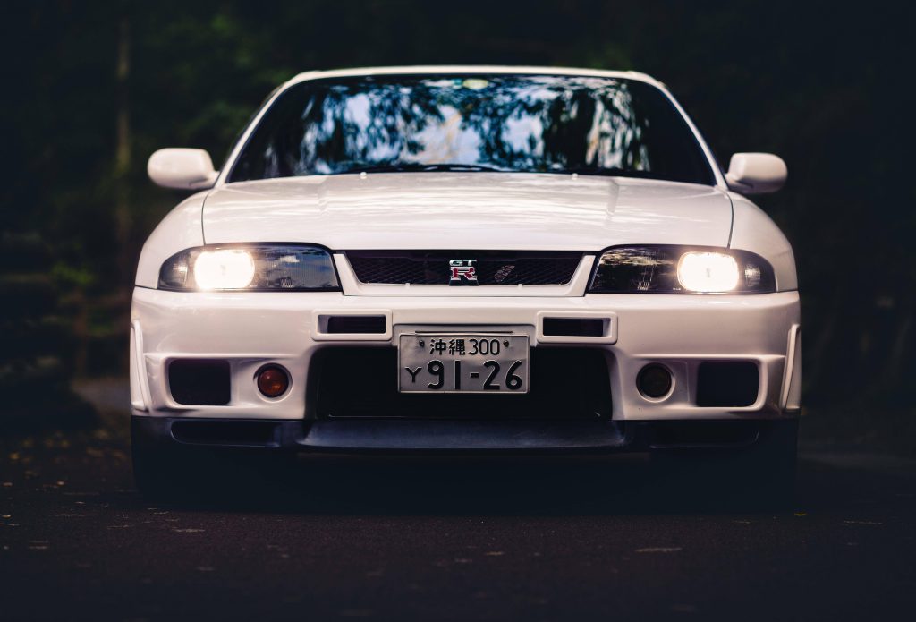 White Nissan Skyline GTR R33 front view with glowing headlights in dark moody JDM wallpaper background
