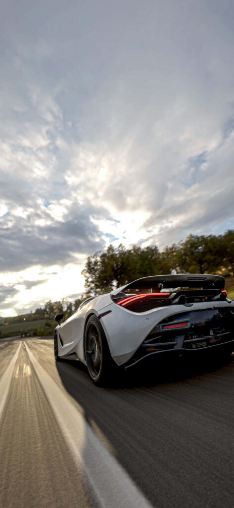 White supercar racing fast on open road with dramatic cloudy sky high quality wallpaper background