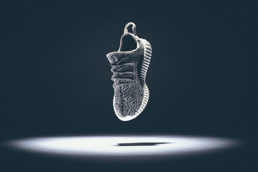 YEEZY sneaker floating above spotlight showcasing sleek modern design on dark wallpaper background