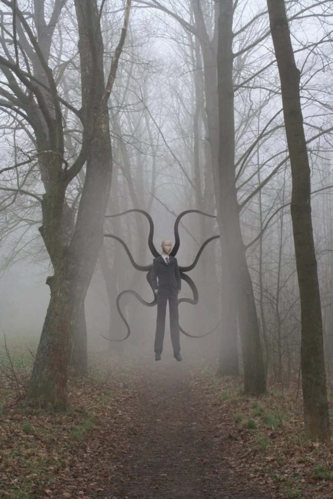 Slender Man in dark suit with tentacles on eerie foggy forest path supernatural horror wallpaper
