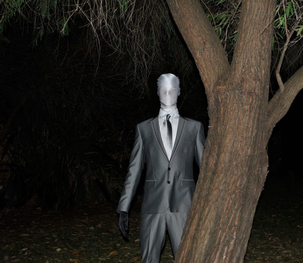 Slender Man in grey suit by dark forest tree eerie horror wallpaper flash photo background