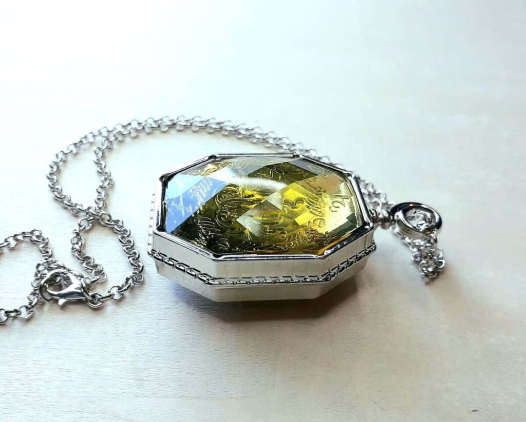 Close-up of Slytherin Locket replica with glowing yellow-green Horcrux gem on neutral backdrop Wallpaper
