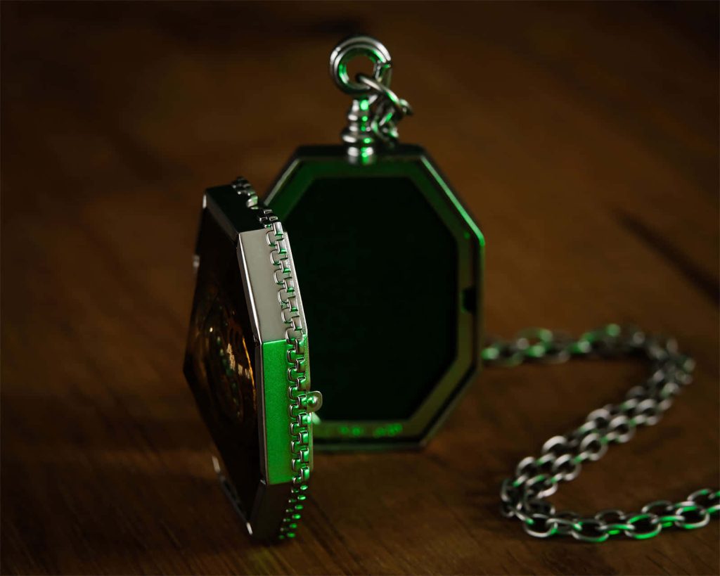 Close-up of Slytherin’s Locket Horcrux glowing green on wooden table Harry Potter wallpaper