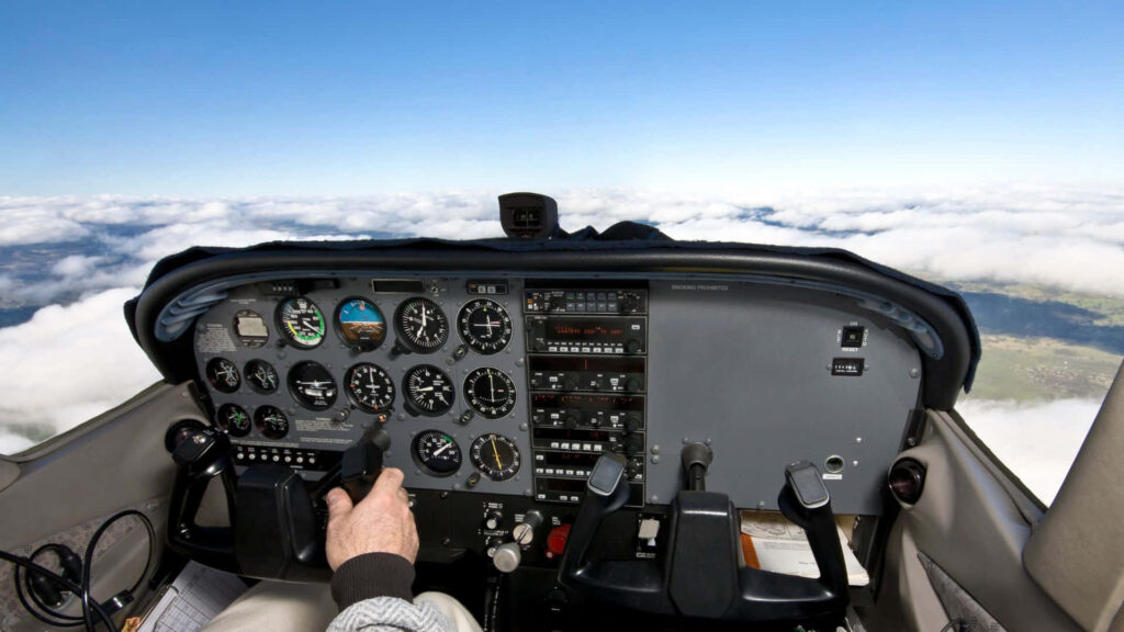 Small aircraft cockpit view above clouds with detailed analog instruments and clear blue sky Wallpaper