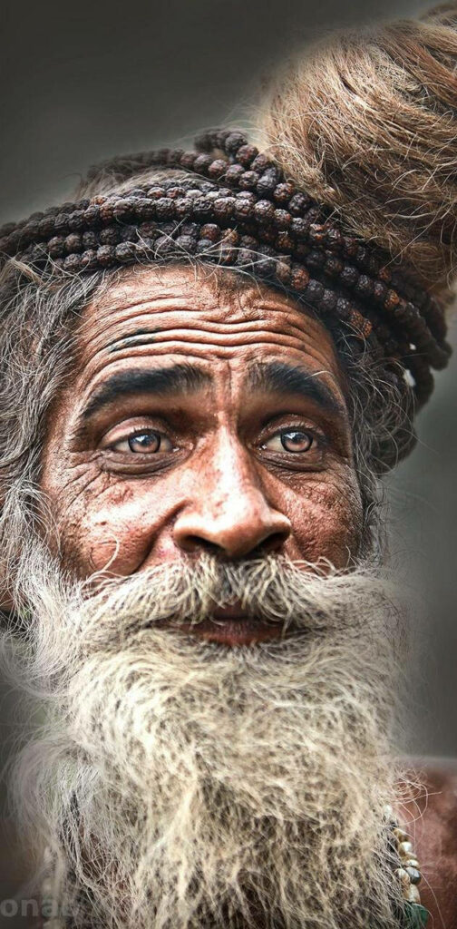 Close-up portrait of smiling Aghori with white beard dreadlocks prayer beads wisdom serenity wallpaper