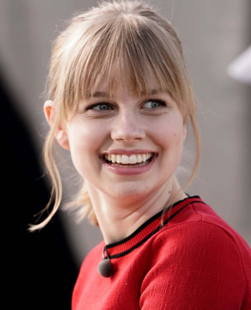 Smiling Angourie Rice in a vibrant red top with cheerful radiant expression wallpaper background