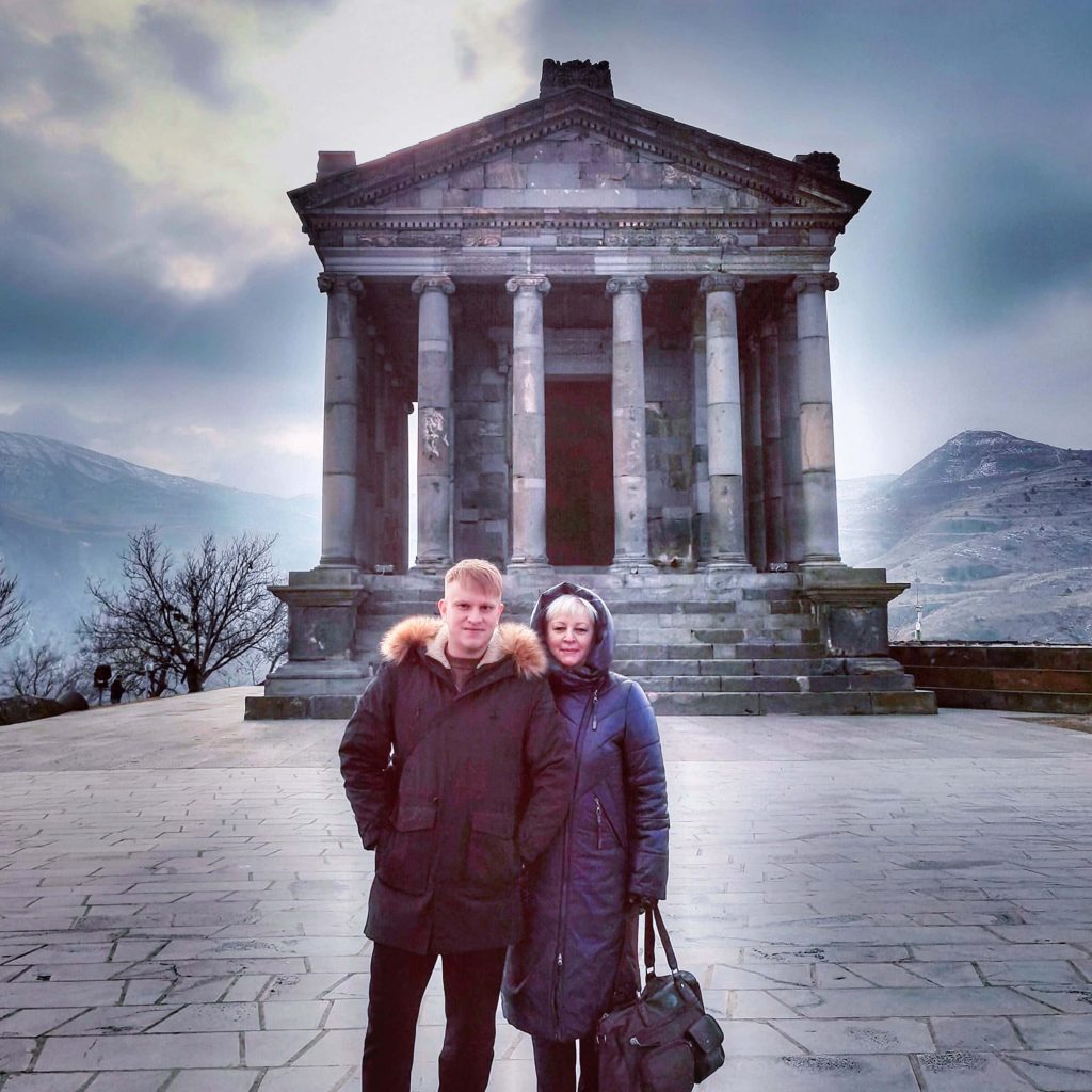 Smiling couple explores ancient Garni Temple Armenia with Hellenistic columns and mountain backdrop Wallpaper