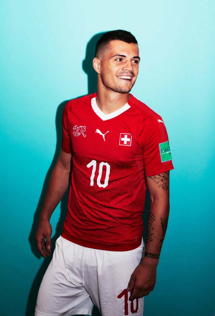 Smiling Granit Xhaka in red number 10 Swiss football kit on vibrant cyan background wallpaper