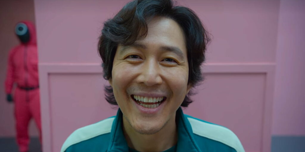 Squid Game wallpaper close-up of Lee Jung-jae as Seong Gi-hun in green tracksuit with pink guard background