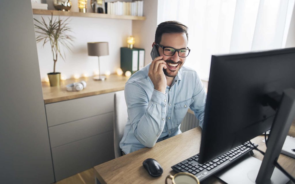 Smiling man with glasses on phone in bright modern minimalist home office workspace background Wallpaper