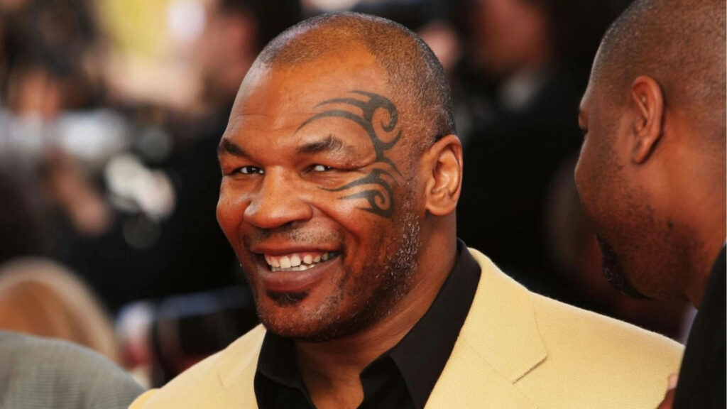 The Joyful Encounter: Legendary Boxer Mike Tyson Grinning Amidst a Blurred Background Wallpaper
