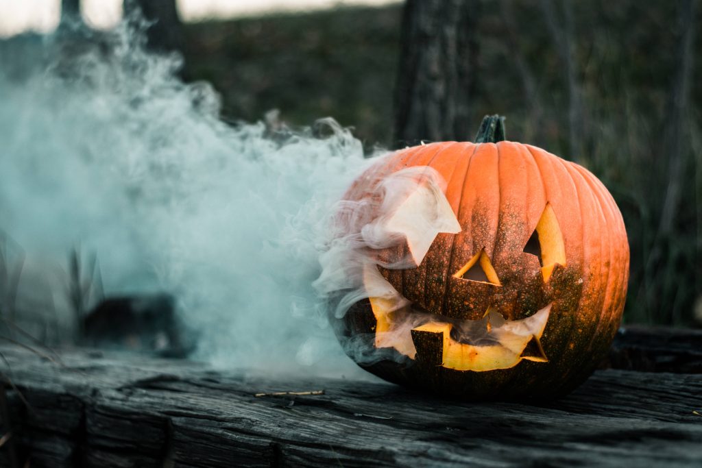 Smoky jack-o-lantern on rustic log emitting fog Halloween pumpkin wallpaper background
