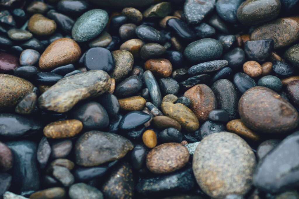 Smooth rounded stones in dark blue grey and brown tones on a sea-washed textured background Wallpaper