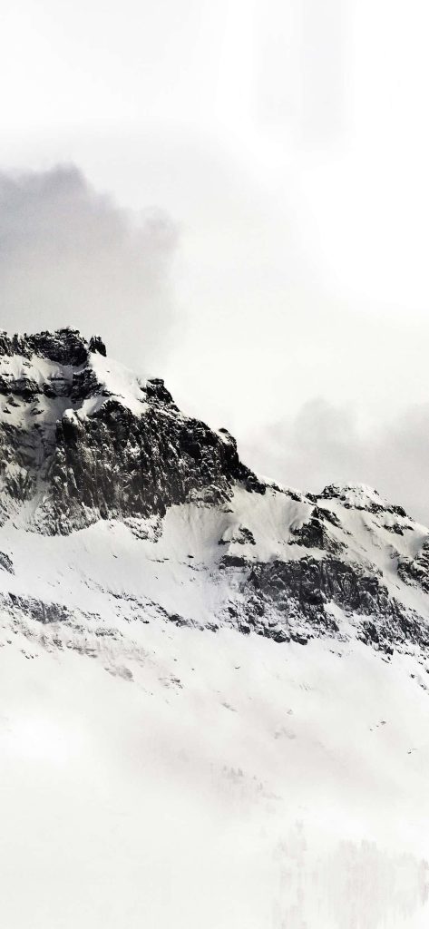 Snow-capped rugged mountain peak with dark rocks under moody winter sky wallpaper background