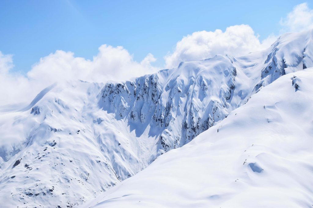 Snow-capped rugged mountain range under clear blue sky with soft clouds alpine landscape wallpaper