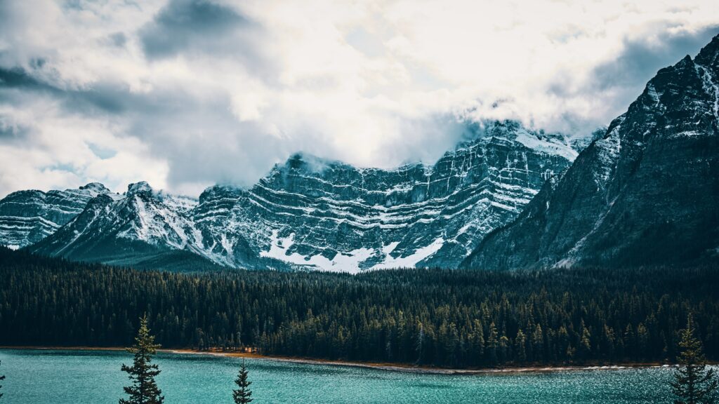 Snow-capped mountains above evergreen forest reflected in turquoise lake vibrant nature wallpaper