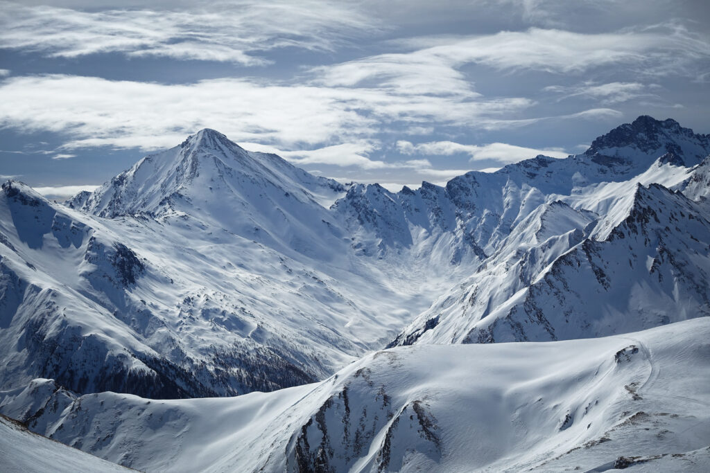 Snow-covered mountain landscape under dramatic swirling clouds capturing winter nature beauty Wallpaper