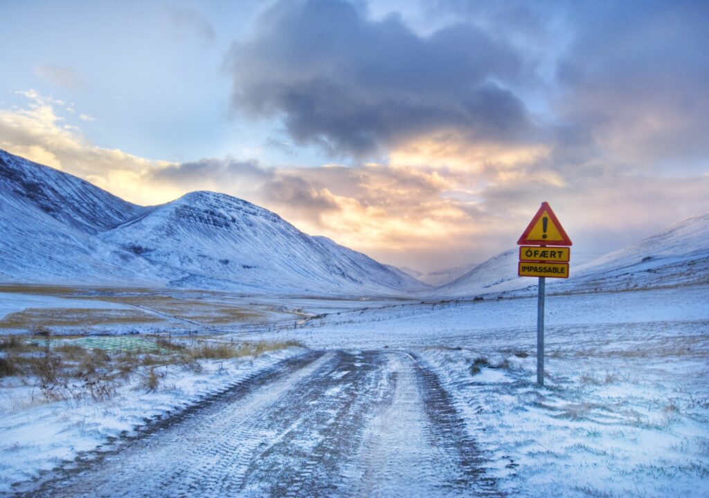 Snow-covered mountain landscape with dramatic clouds and a warning road sign for safety Wallpaper
