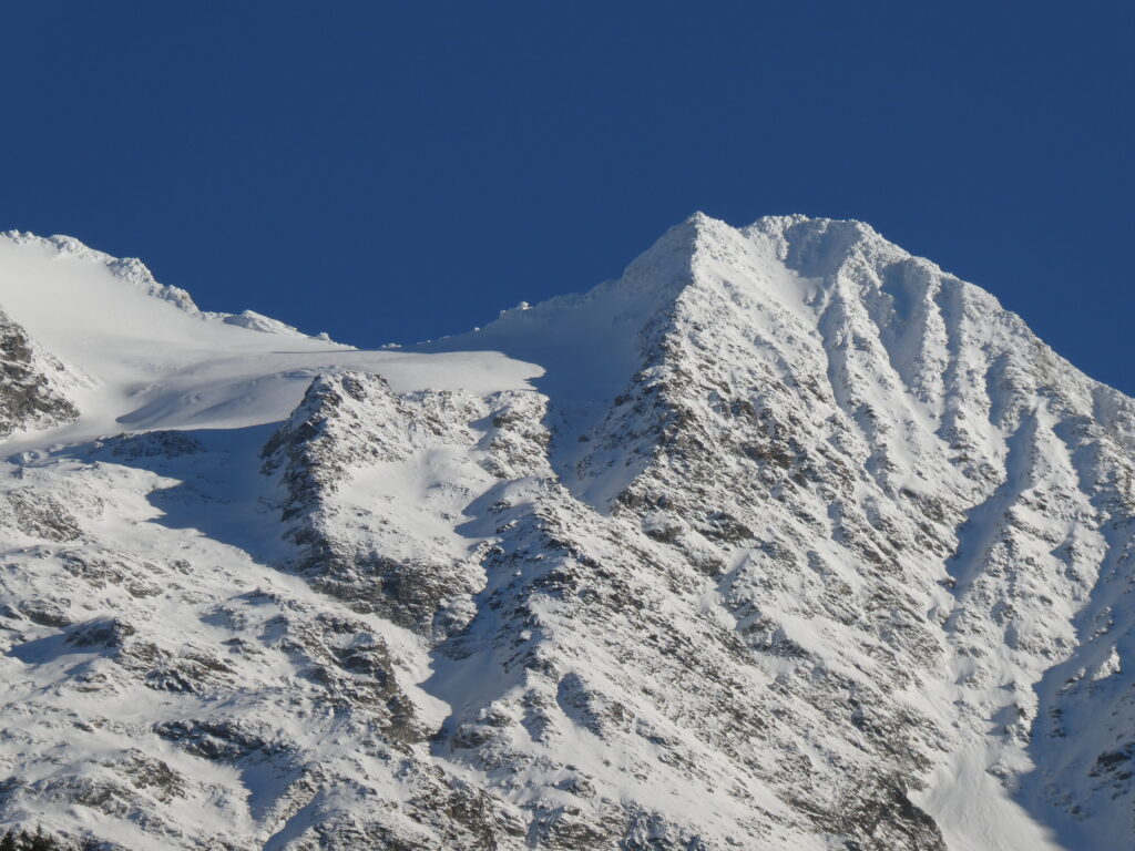 Snow-covered mountain peak with sharp slopes and rugged rocks under deep blue winter sky wallpaper