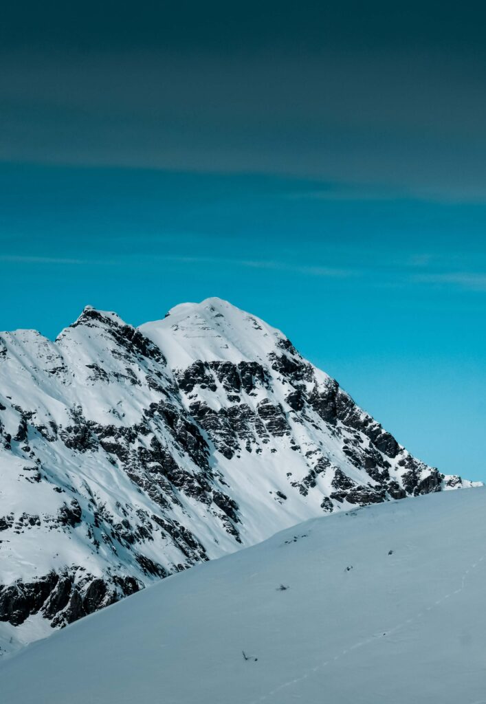 Snow-covered alpine peaks with rugged rocks and smooth slopes under a clear blue sky wallpaper