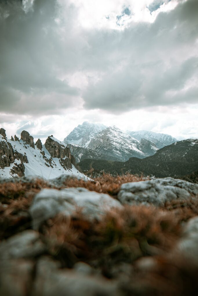 Snow-capped mountain peaks under dramatic cloudy sky with rugged foreground landscape view Wallpaper