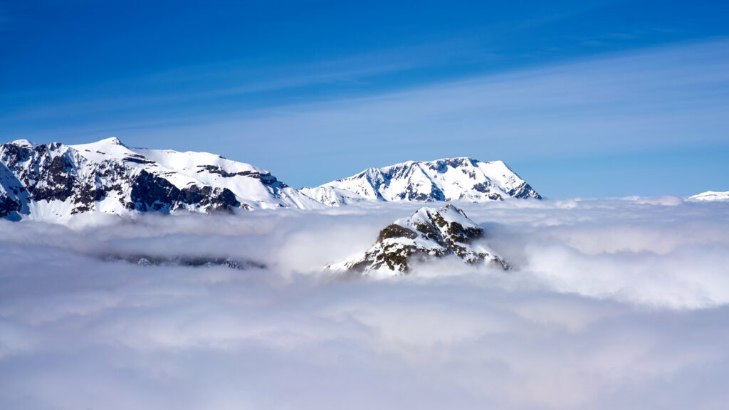 Snowcapped mountain peaks above clouds under vivid blue sky serene nature wallpaper background