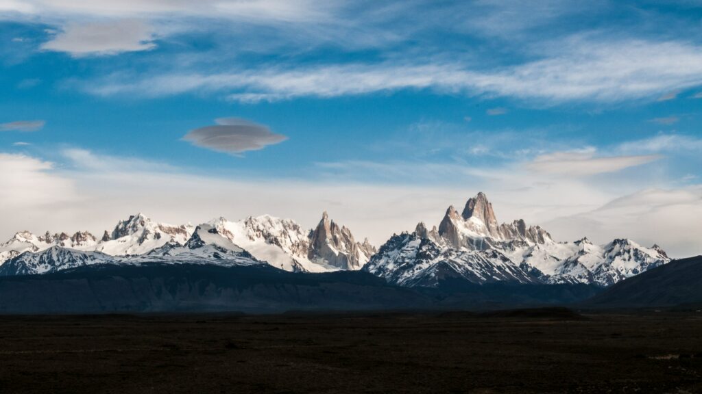 Snow-capped mountain range under vibrant blue sky with wispy clouds serene landscape wallpaper
