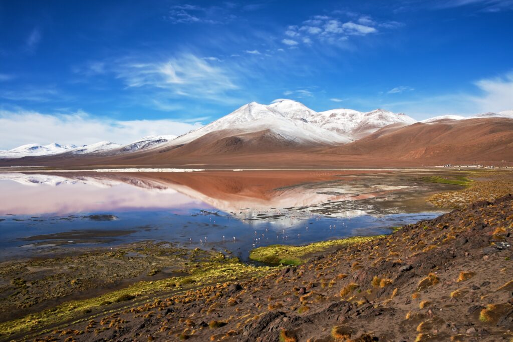 Snow-capped mountain peak reflected in clear lake with vibrant earthy tones and dramatic sky background Wallpaper