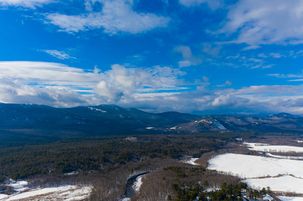 Snow-capped mountains with dense forest and winding river under vivid blue sky wallpaper background