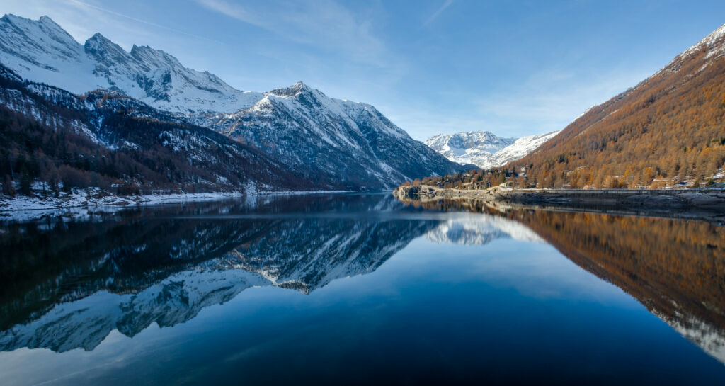 Snow-capped mountains reflected in a serene lake with spring foliage and a clear blue sky Wallpaper