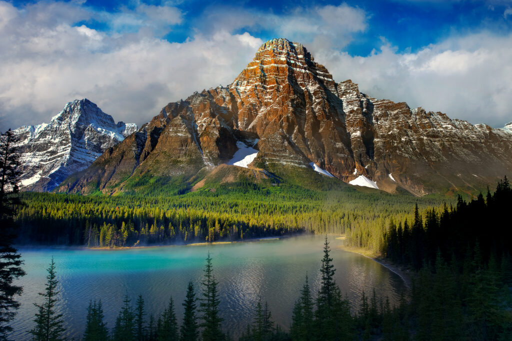 Snow-capped mountains reflected in turquoise lake surrounded by green forest under blue sky wallpaper