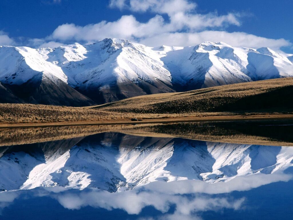 Snow-capped mountains reflected in a clear lake under vivid blue sky winter wallpaper background