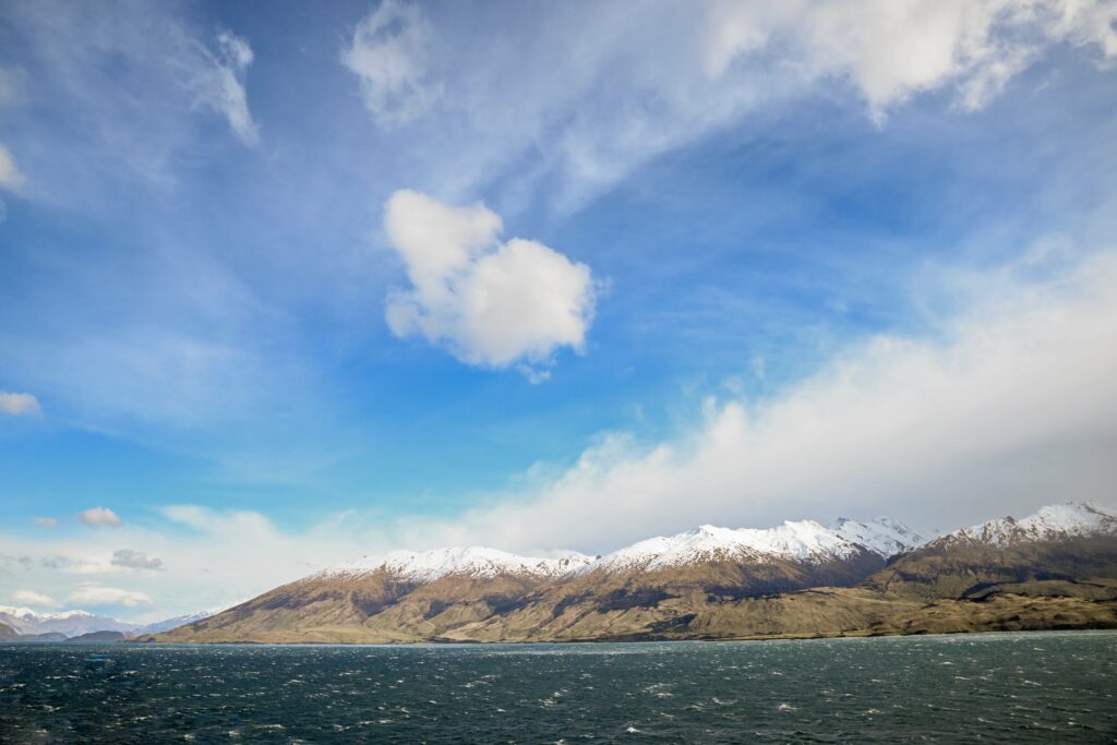 Snow-capped mountains above deep blue sea under soft clouds serene natural landscape wallpaper