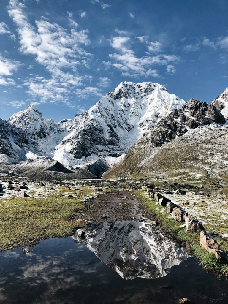 Snow-capped mountains reflect in a tranquil lake with rugged rocks under a vivid blue sky wallpaper