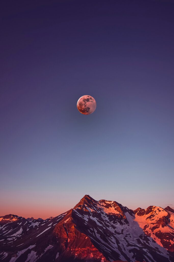 Snow-capped mountains at sunset with a glowing full moon in a serene twilight sky wallpaper