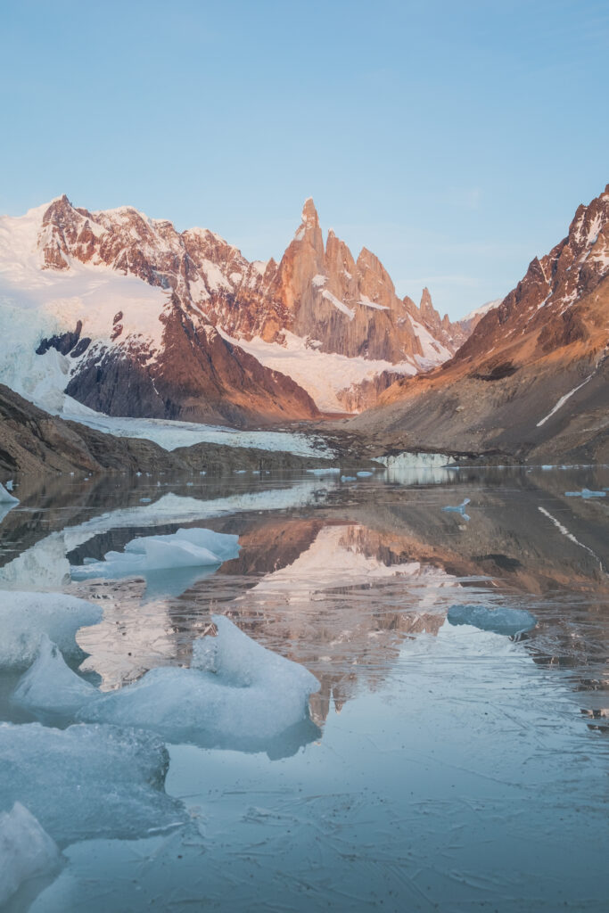 Snow-capped jagged peaks reflecting in a frozen lake with floating ice and golden hues wallpaper